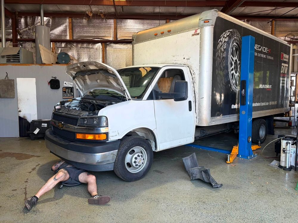 Chevy Express box truck with a technician underneath during AC system replacement in North Little Rock, Arkansas